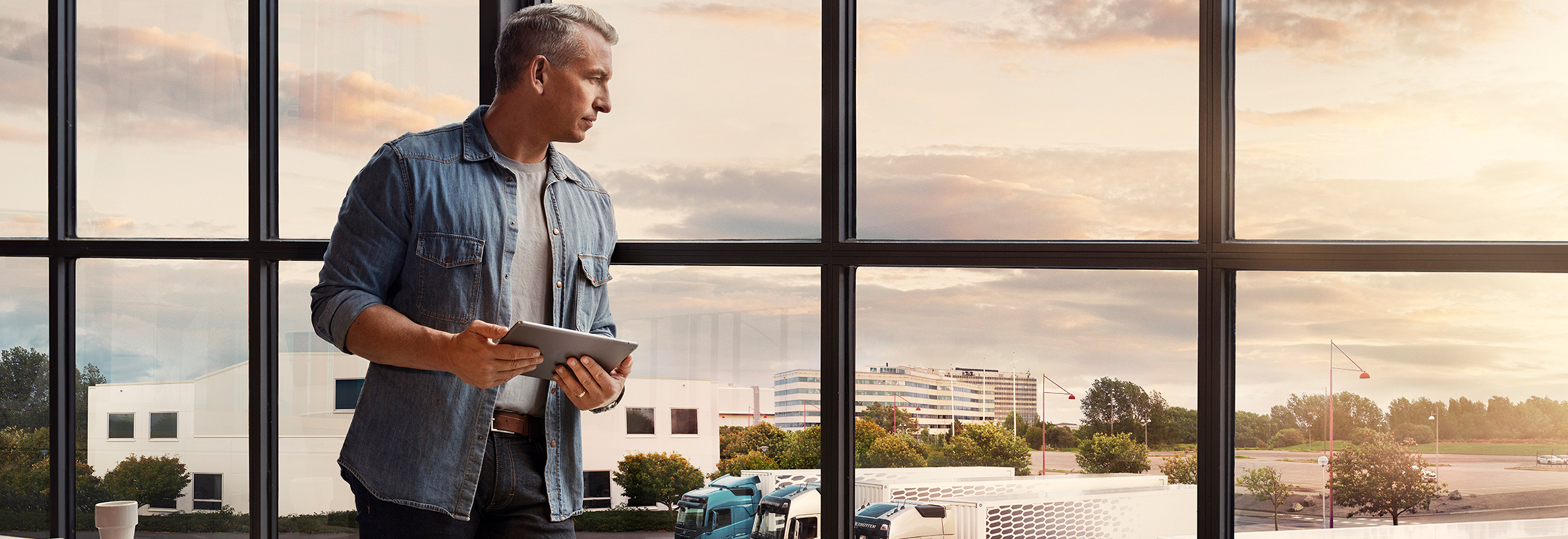 Čovek koji drži tablet stoji pored prozora i gleda u svoj vozni park kamiona